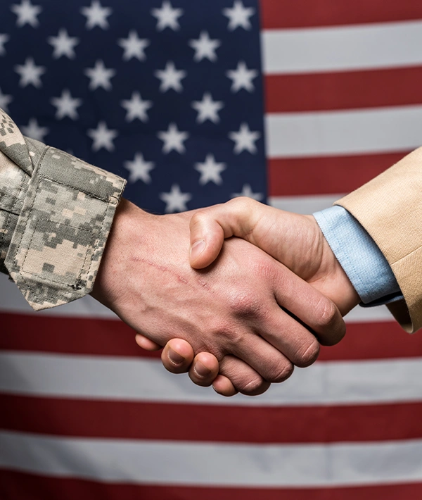 Handshake between military and civilian professionals in front of the American flag, symbolizing government contracting readiness